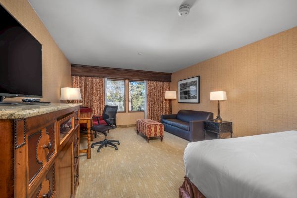 A hotel room with a bed, desk, chair, television, lamps, and curtains.
