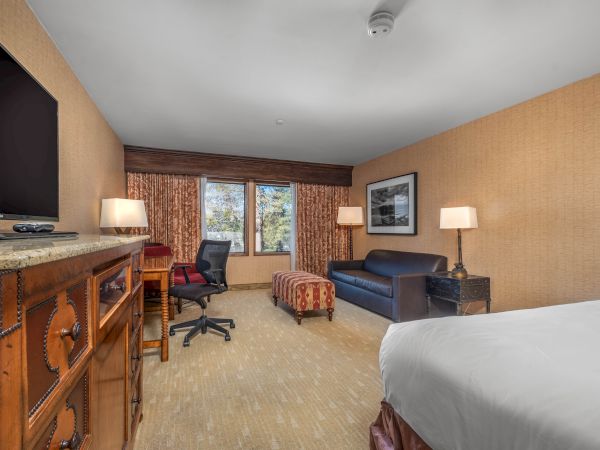 A hotel room with a bed, desk, chair, television, lamps, and curtains.