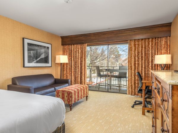 This is a hotel room with a bed, sofa, desk, chairs, and a balcony with a view.