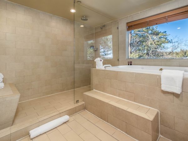 Modern bathroom with a glass shower, bathtub, and a window with a view.