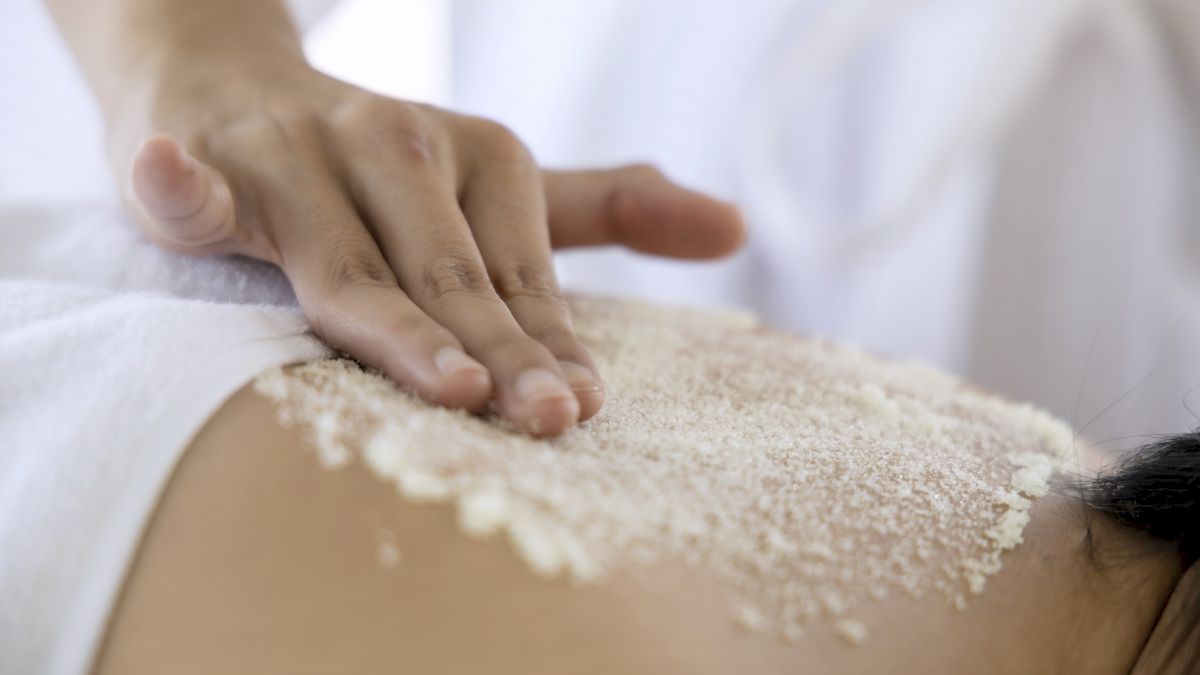 A person receiving a massage with powder on their back, while a hand applies it gently.