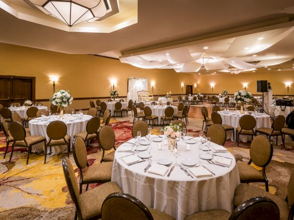 An elegant banquet hall set up with round tables, chairs, and floral centerpieces.