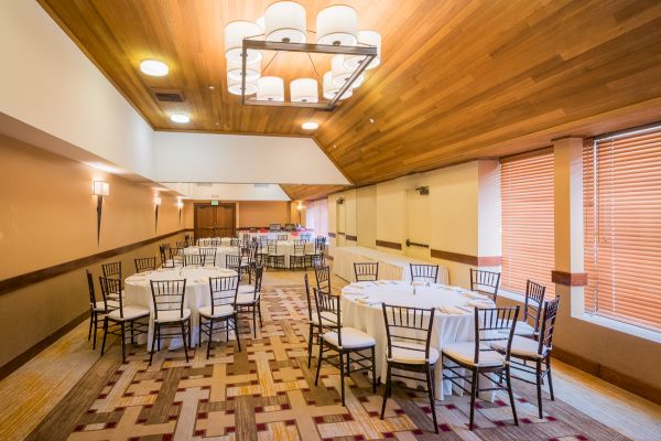 An empty banquet hall with arranged chairs and tables, pendant lights above.