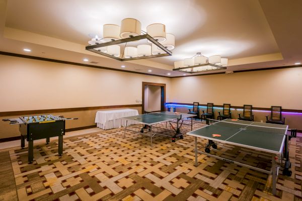 A game room with a ping pong table, foosball, carpeted floor, and overhead lighting.