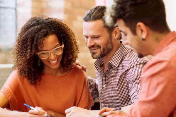 Three people are collaborating over a document, engaged and smiling.