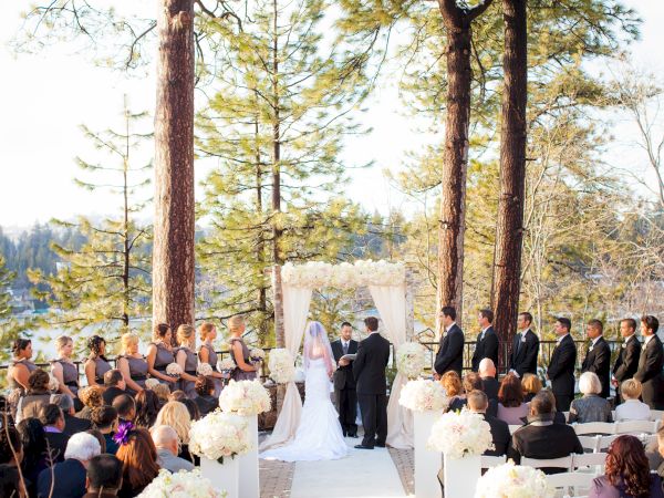 An outdoor wedding ceremony with guests, a couple at the altar, and scenic lake backdrop.