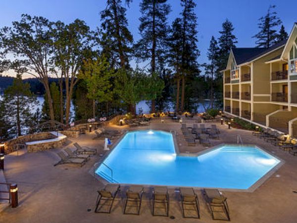 A tranquil pool by a lake adjacent to a hotel at dusk.