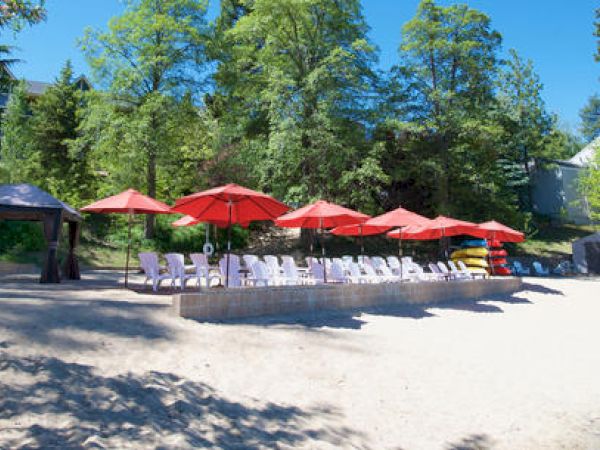 Outdoor seating with red umbrellas, white chairs on sand, surrounded by trees.