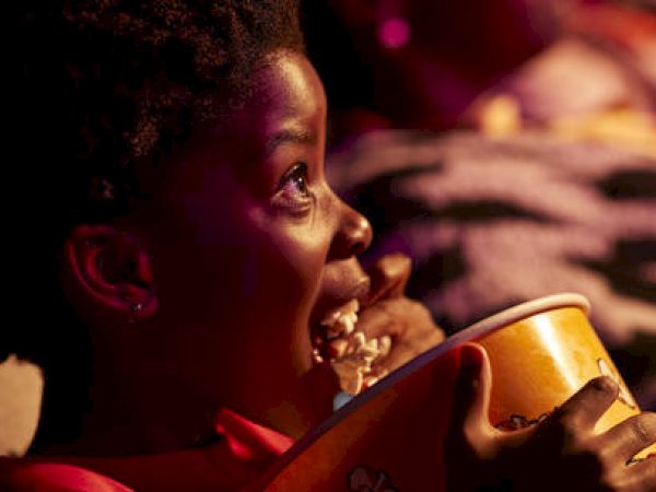 A child eating popcorn, watching a movie, looking up with an expression of awe.