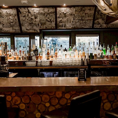 An array of bottles lines the bar counter, with stools and moody lighting.