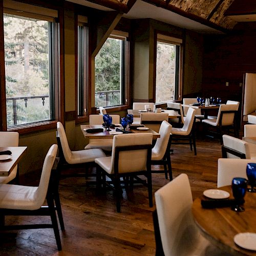 Elegant dining area with tables set, blue glassware, amidst wood interiors.