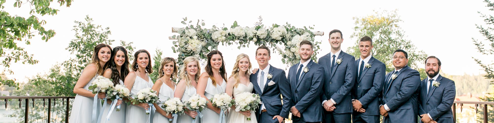 A wedding party posing outdoors with bridesmaids in blue and groomsmen in suits.