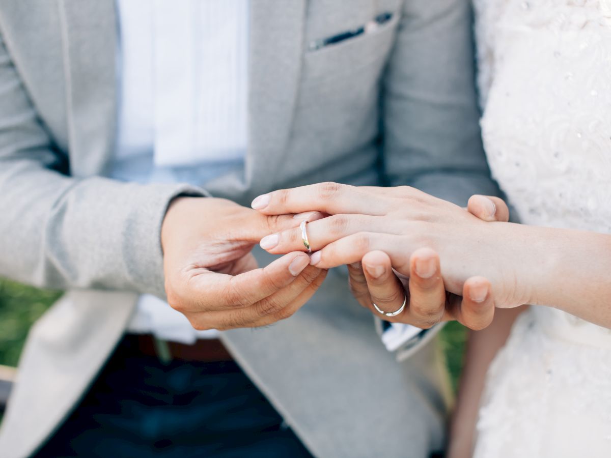 A person is placing a wedding ring on another's finger, suggesting a marriage ceremony or engagement outdoors.