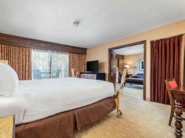 This image shows a hotel room with a bed, curtains, a TV, and a separate seating area with a sofa.