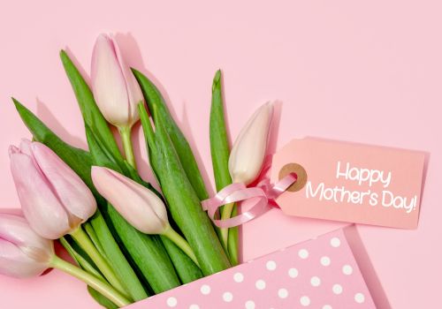 Pink tulips in a polka dot envelope with a "Happy Mother's Day" tag on a pink background.