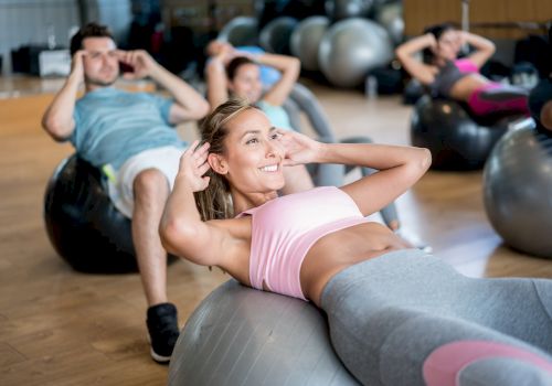People are exercising on stability balls in a gym, performing abdominal workouts and smiling.