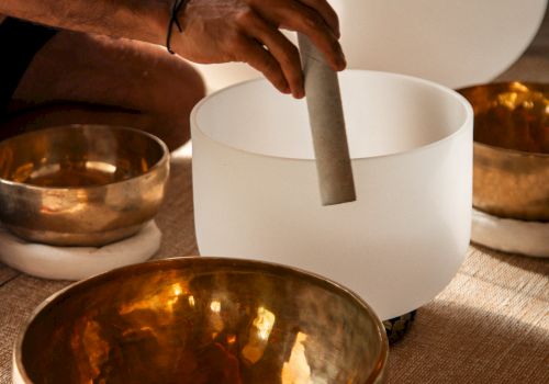 A hand is playing crystal and brass singing bowls, often used for meditation and sound healing practices.