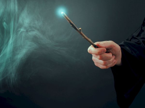 A person holding a glowing wand with a misty, magical effect surrounding it against a dark background.