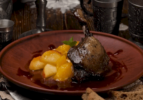 The image shows a rustic setting with lit candles, goblets, and a plate of cooked meat with potatoes, creating a medieval dining atmosphere.