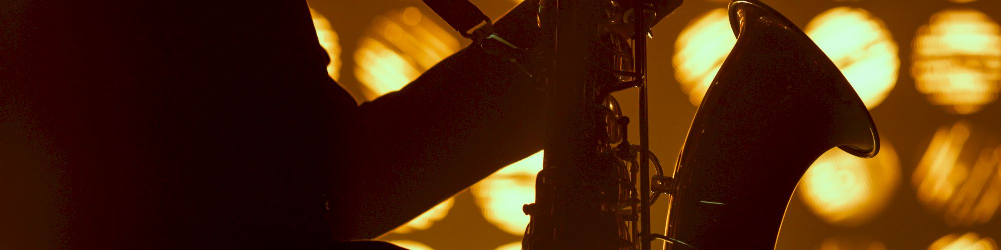 Silhouette of a saxophonist playing, with warm, circular lights in the background creating a dramatic and artistic scene.