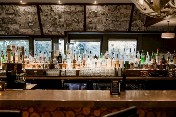 A bar with a wide selection of liquor bottles, glasses, and taps, set against a rustic interior with warm lighting.