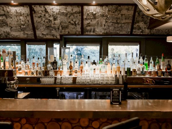 A bar with a wide selection of liquor bottles, glasses, and taps, set against a rustic interior with warm lighting.