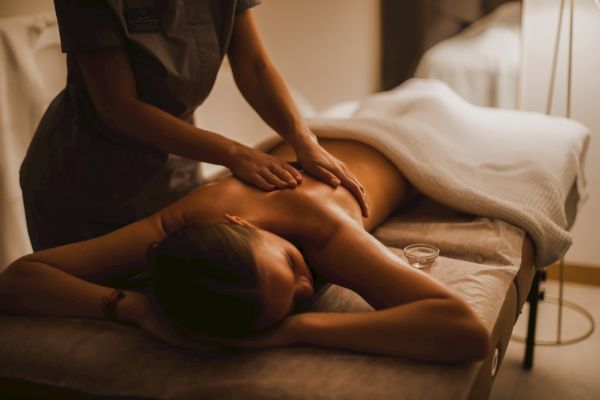 A person is receiving a massage in a spa setting, lying face down on a table with a white towel covering their lower body.
