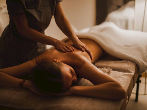 A person is receiving a massage in a spa setting, lying face down on a table with a white towel covering their lower body.