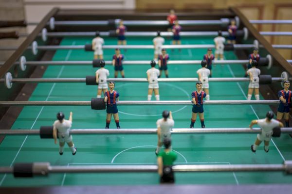 A foosball table with players in blue and red and white uniforms, set on a green playing field in a casual setting.