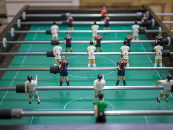A foosball table with players in blue and red and white uniforms, set on a green playing field in a casual setting.