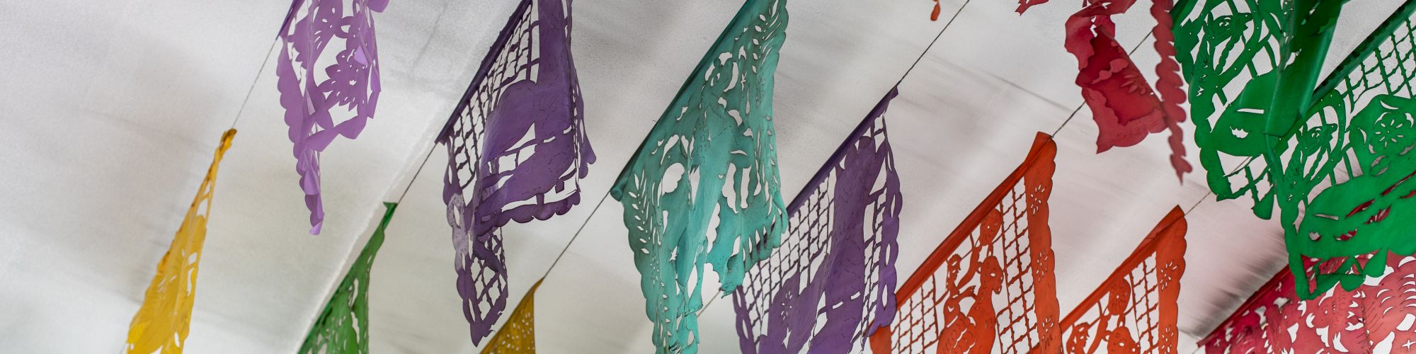 Colorful papel picado banners are hanging from a ceiling in various colors, creating a festive atmosphere.