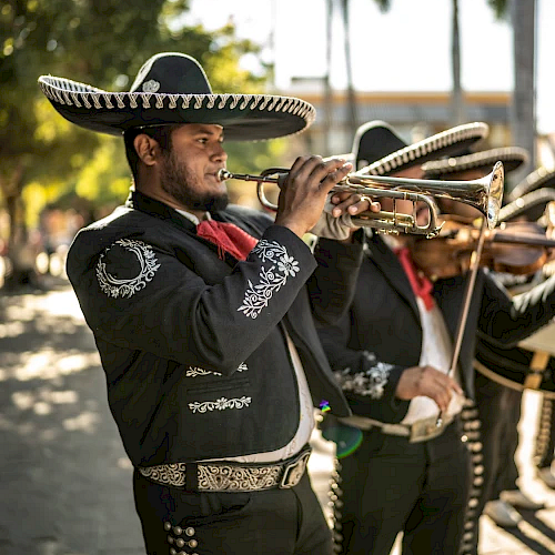 A mariachi band member plays the trumpet outdoors, wearing traditional attire with a sombrero.