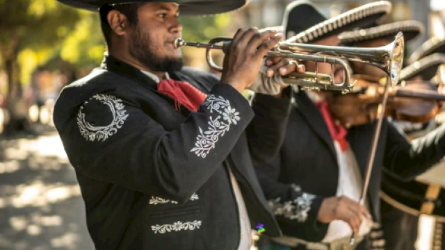 A mariachi band member plays the trumpet outdoors, wearing traditional attire with a sombrero.