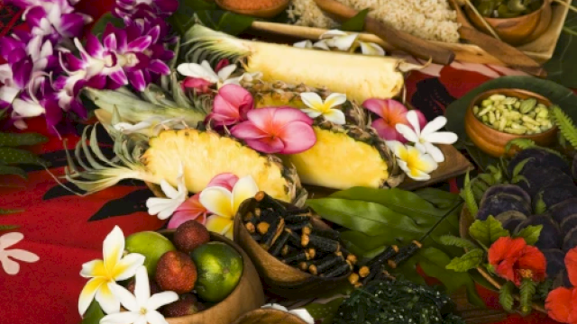 A vibrant spread of tropical fruits, colorful flowers, and assorted dishes on a red cloth, conveying a festive and exotic atmosphere.